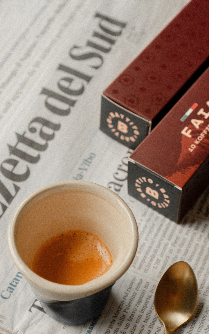 Espresso van Battito op een krant van Gazzetta del Sud met twee doosjes Battito Faia koffiecapsules voor Nespresso-koffiecupmachines en een lepel