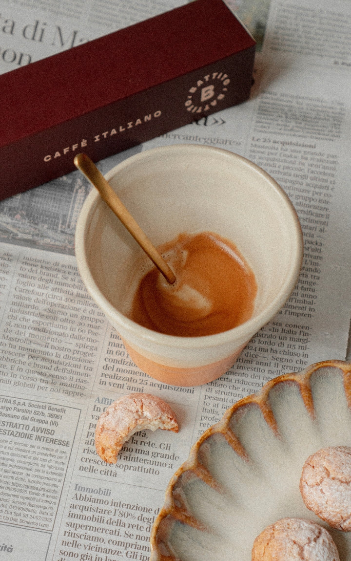 Lungo van Battito in een kopje op een krant met een bord met amaretti en een doos Stella koffiecapsules voor een Nespresso-koffiecupmachine